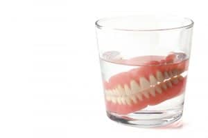 Set of dentures in cup of cleaning liquid