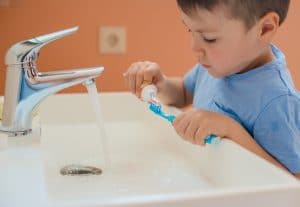 Young boy putting toothpaste on his toothbrush to brush his teeth.