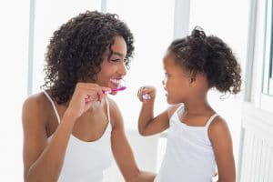 African American mother with her young daughter brushing their teeth